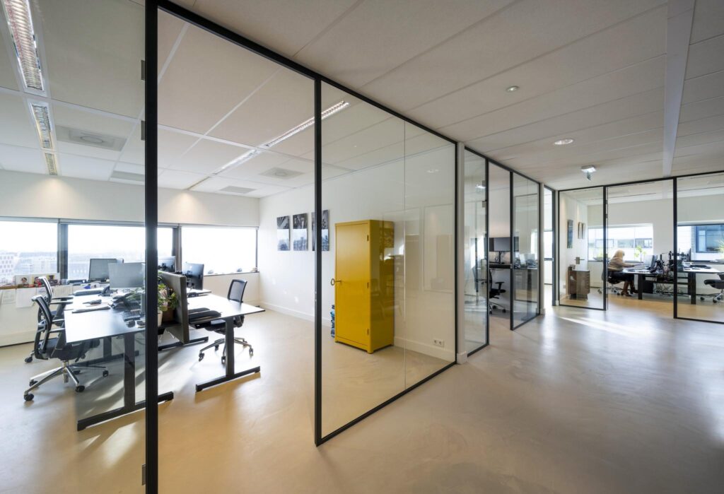 Moderne kantoorruimte op Rietlandpark met glazen wanden, werkplekken en een opvallende gele kast.