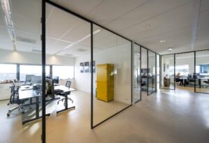 Moderne kantoorruimte op Rietlandpark met glazen wanden, werkplekken en een opvallende gele kast.