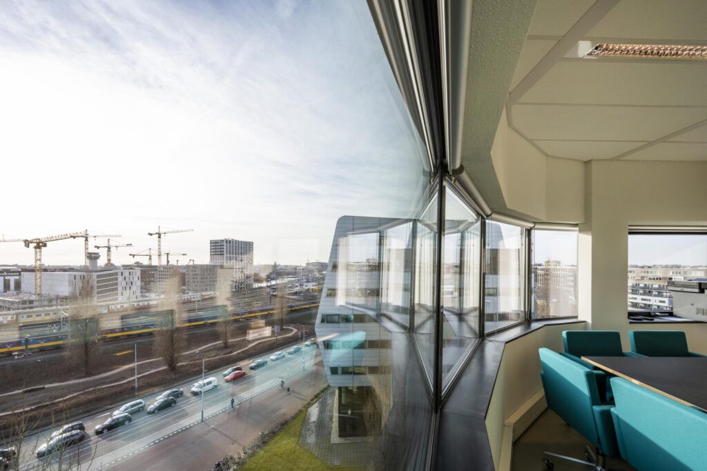 Vergaderruimte met uitzicht op Rietlandpark, modern stadsverkeer en bouwwerkzaamheden met hijskranen.