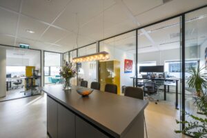 Modern kantoorinterieur in Rietlandpark met glazen vergaderruimtes, een hoge tafel, bloemenvaas en sfeerverlichting.