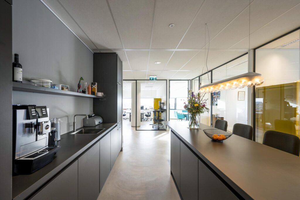 Moderne kantoorkeuken met koffiezetapparaat, bloemenvaas en zicht op open werkruimtes in Rietlandpark.