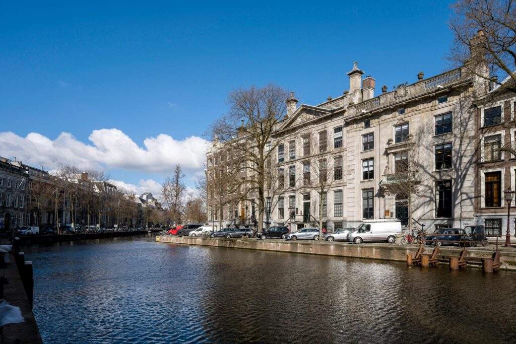 Canal view of Herengracht in Amsterdam with historic buildings and parked cars along the water.