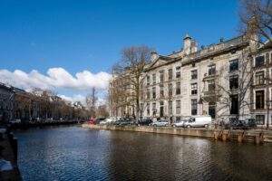 Canal view of Herengracht in Amsterdam with historic buildings and parked cars along the water.