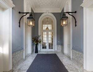 Elegant entrance hallway of Herengracht building with marble floors, classic wall lamps, and a large flower arrangement.