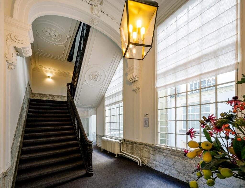 Elegant staircase with ornate ceiling and large windows in a historic Herengracht building.