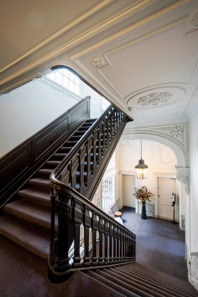 Elegant staircase with dark wood railings and ornate ceiling details in a historic Herengracht building.