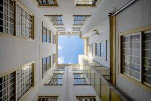 Upward view of a lightwell in the Herengracht building, showing symmetrical white walls and window frames against a blue sky.