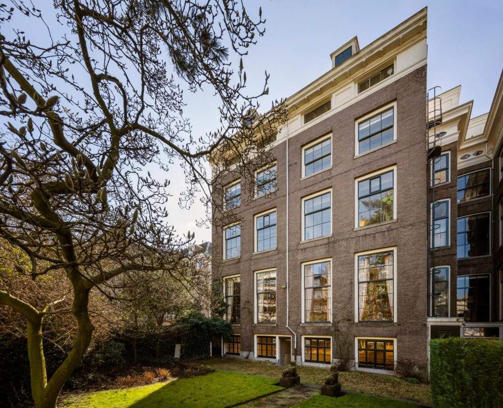 Back view of a historic Herengracht canal house with large windows and a garden with trees.