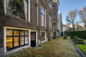 Historic canal house with large windows and moss-covered courtyard on Herengracht in Amsterdam.