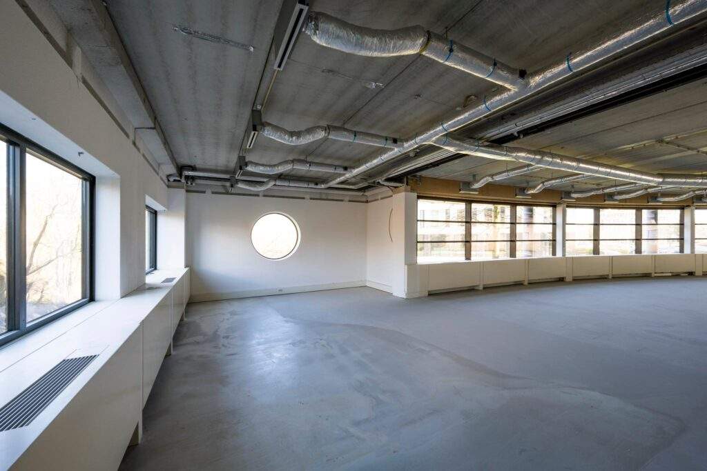 Leeg, industrieel ogend kantoorinterieur aan de Wegalaan met zichtbare ventilatiebuizen en grote raampartijen.