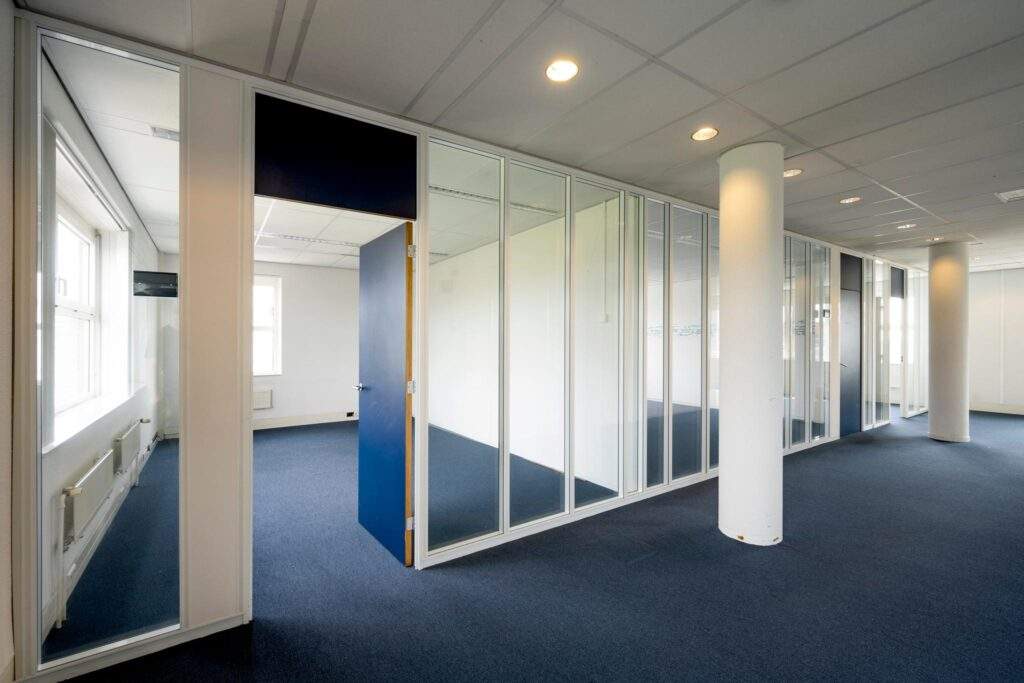 Kantoorgang met glazen scheidingswanden, blauwe deuren en blauwe vloerbedekking.