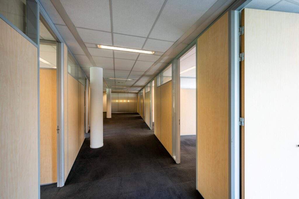 Een moderne kantoorgang met houten scheidingswanden en donkere vloerbedekking.