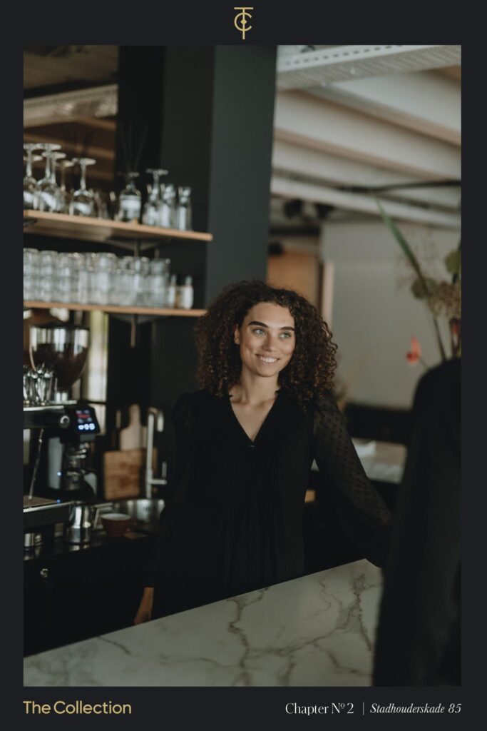 Smiling woman standing behind a marble counter at a stylish café on Stadhouderskade 85.