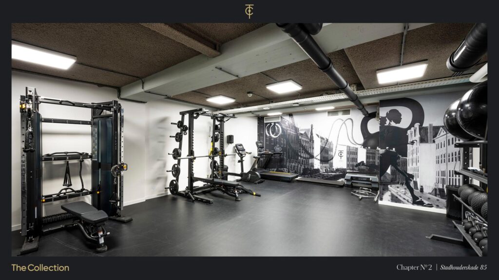 Modern fitness room at Stadhouderskade 85 equipped with strength and cardio machines and a mural featuring Amsterdam architecture.