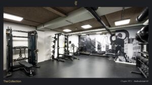 Modern fitness room at Stadhouderskade 85 equipped with strength and cardio machines and a mural featuring Amsterdam architecture.