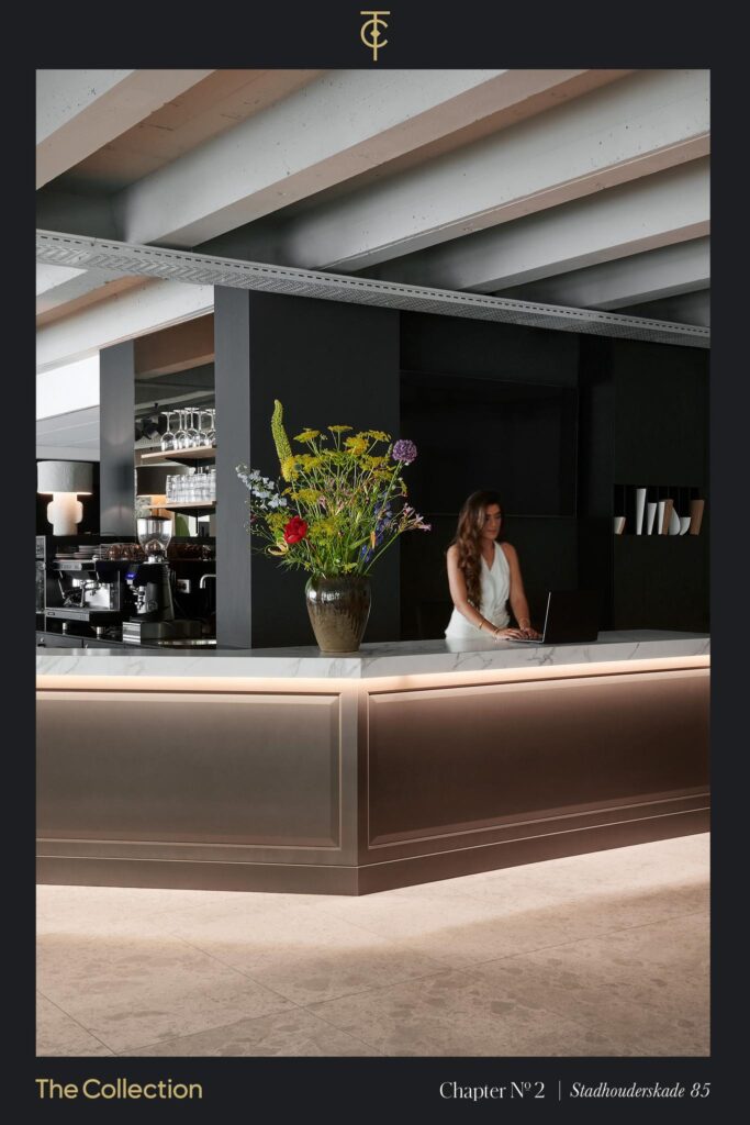 Modern reception area at Stadhouderskade 85 with a marble counter, floral arrangement, and a woman working on a laptop.