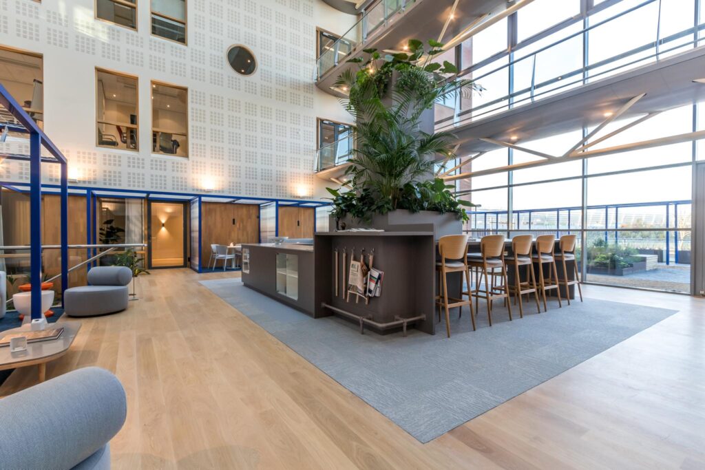 Modern ingerichte lounge- en werkruimte in een kantoor aan de Kabelweg met veel daglicht en groene planten.