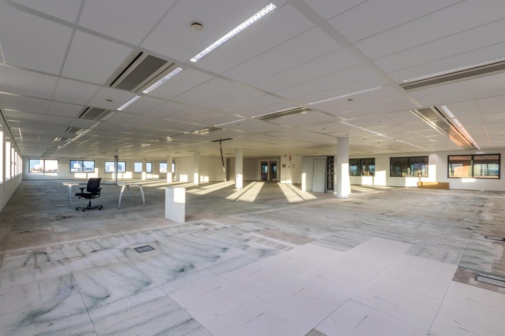 Leegstaand kantoorpand aan de Kabelweg met systeemplafond, ramen rondom en losse bureaus.