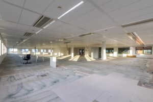 Leegstaand kantoorpand aan de Kabelweg met systeemplafond, ramen rondom en losse bureaus.