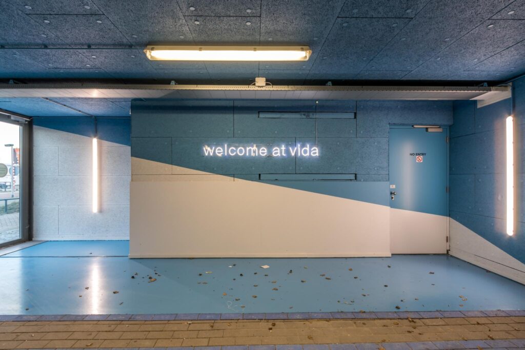 Blauw-witte entree met neontekst "welcome at vida" en een gesloten deur met "no entry"-bordje.