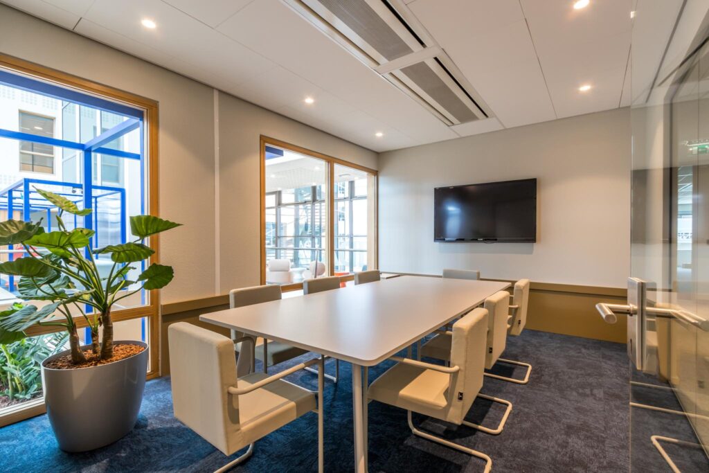 Moderne vergaderruimte aan de Kabelweg met een lange tafel, acht stoelen, een flatscreen en grote ramen met uitzicht op de binnenplaats.