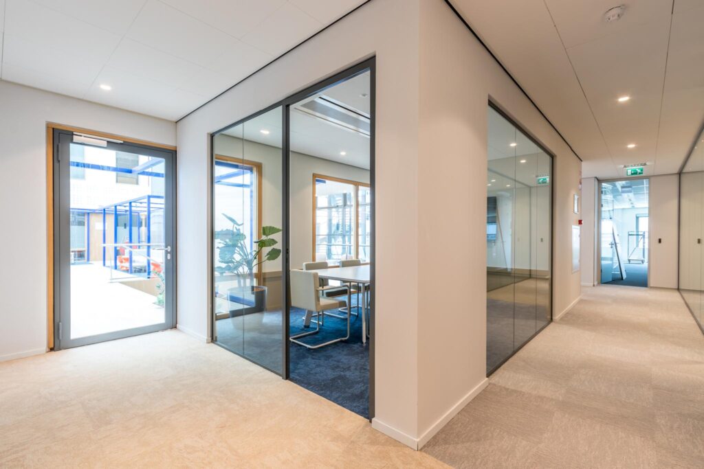 Moderne kantoorruimte aan de Kabelweg met glazen vergaderruimtes en een helder verlichte gang.