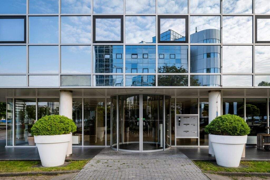 Hoofdentree van een modern kantoorgebouw aan de Hogehilweg met glazen gevel en draaideur.