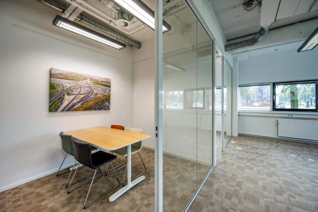Vergaderruimte met glazen wand, houten tafel, vier stoelen en een wandfoto van knooppunt op de Hogehilweg.