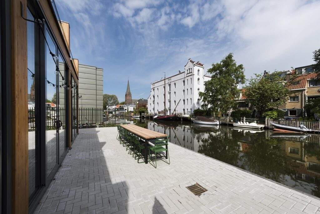 Terras aan de Nieuwendammerkade met uitzicht op het water, boten en historische gebouwen, waaronder een witte pakloods.