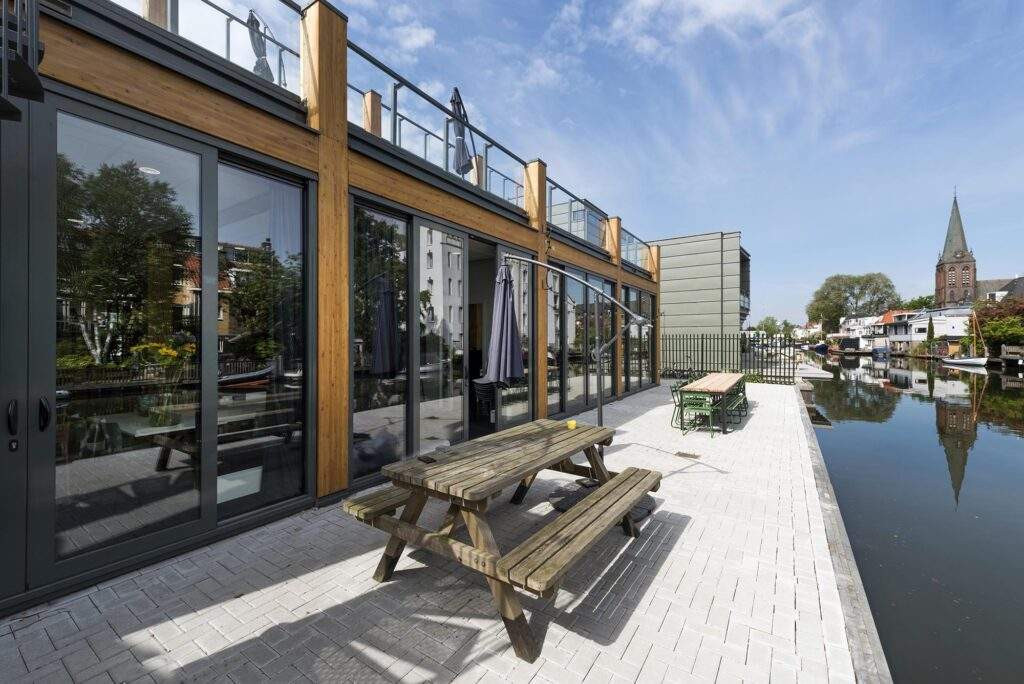 Moderne woning aan de Nieuwendammerkade met houten gevel, grote ramen en terrastafels aan het water.