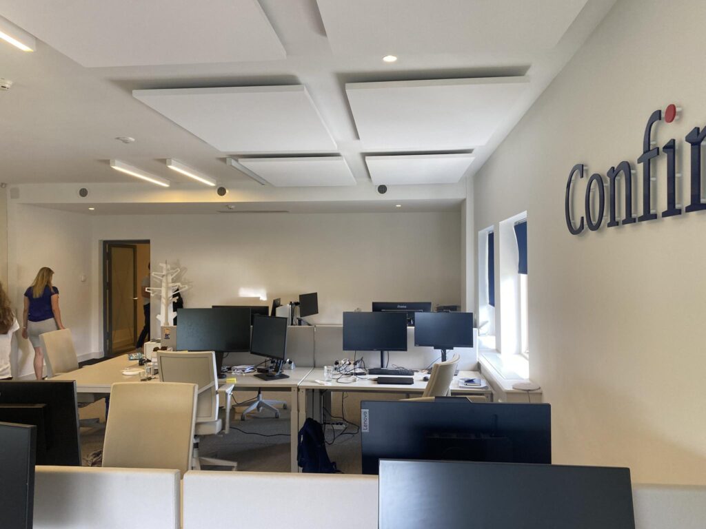Moderne kantooruimte aan de Herengracht met werkplekken, beeldschermen en het logo van Confini op de muur.