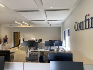 Moderne kantooruimte aan de Herengracht met werkplekken, beeldschermen en het logo van Confini op de muur.