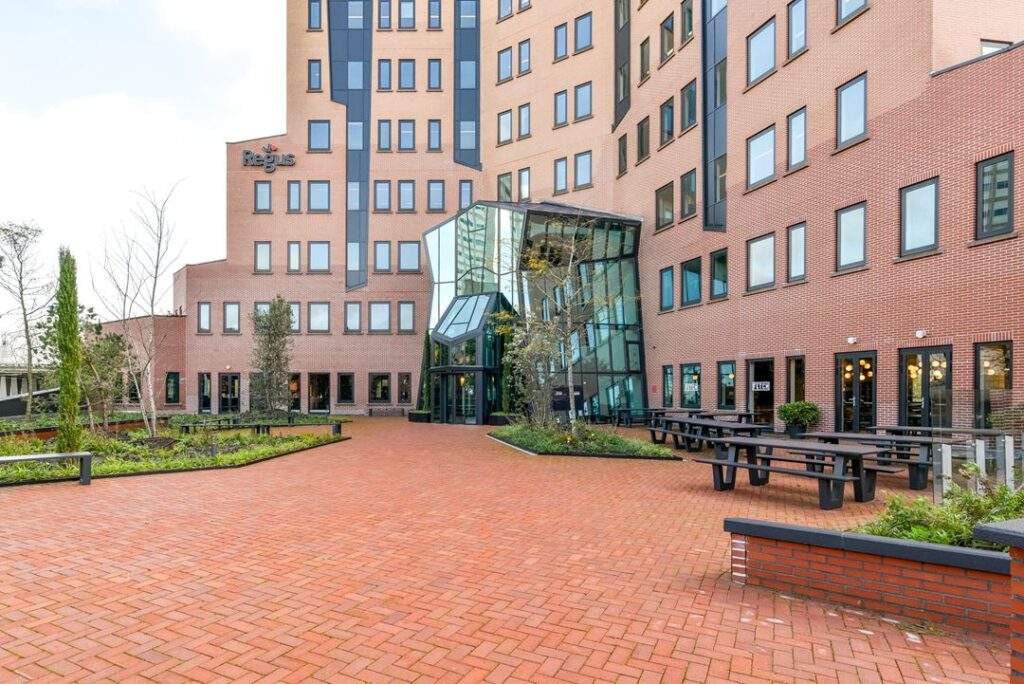 Vooraanzicht van het Regus-kantoorgebouw aan de Kingsfordweg met glazen entree en een betegeld plein met picknicktafels.
