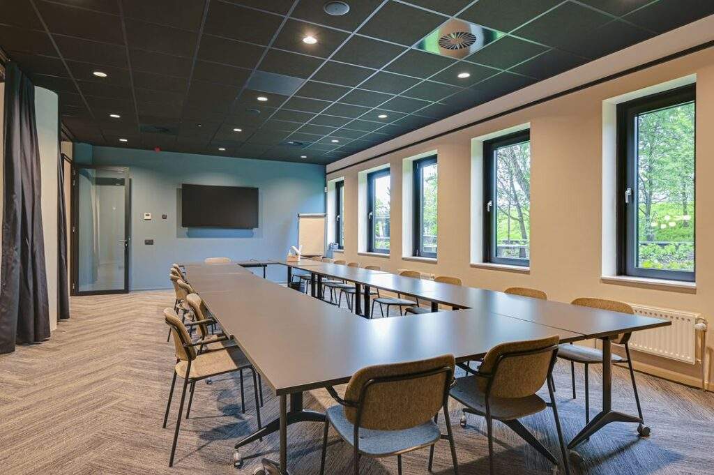Moderne vergaderruimte aan de Kingsfordweg met een grote tafelopstelling, meerdere stoelen, een flatscreen en grote ramen met uitzicht op groen.