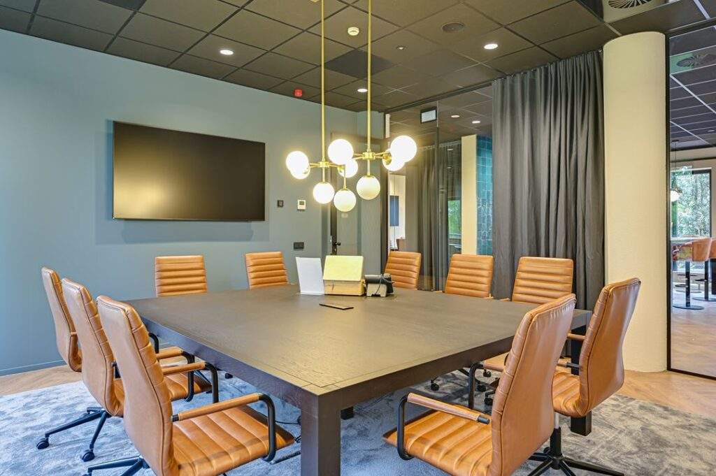 Moderne vergaderruimte aan de Kingsfordweg met een vierkante tafel, cognackleurige stoelen en een grote flatscreen aan de muur.
