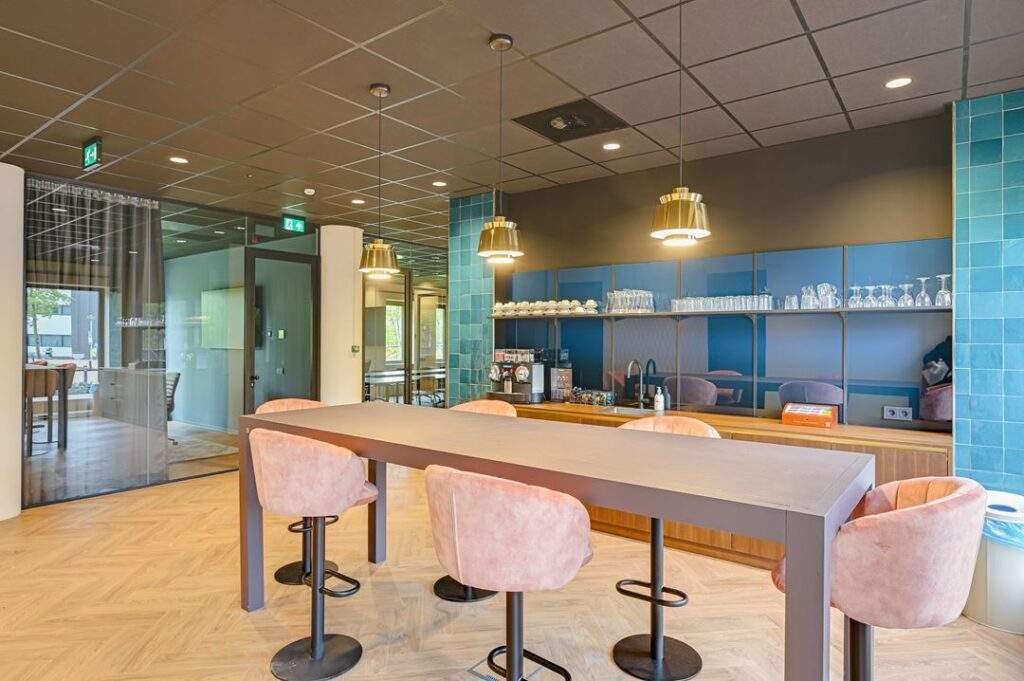Moderne kantoorkeuken aan de Kingsfordweg met hoge tafel, roze barkrukken en koffiecorner.
