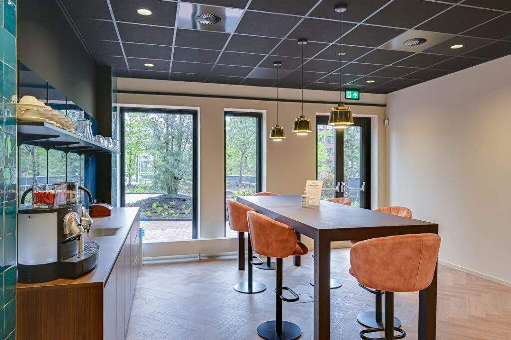 Moderne koffiehoek met hoge tafel, fluwelen barkrukken en zicht op een groene buitenomgeving aan de Kingsfordweg.