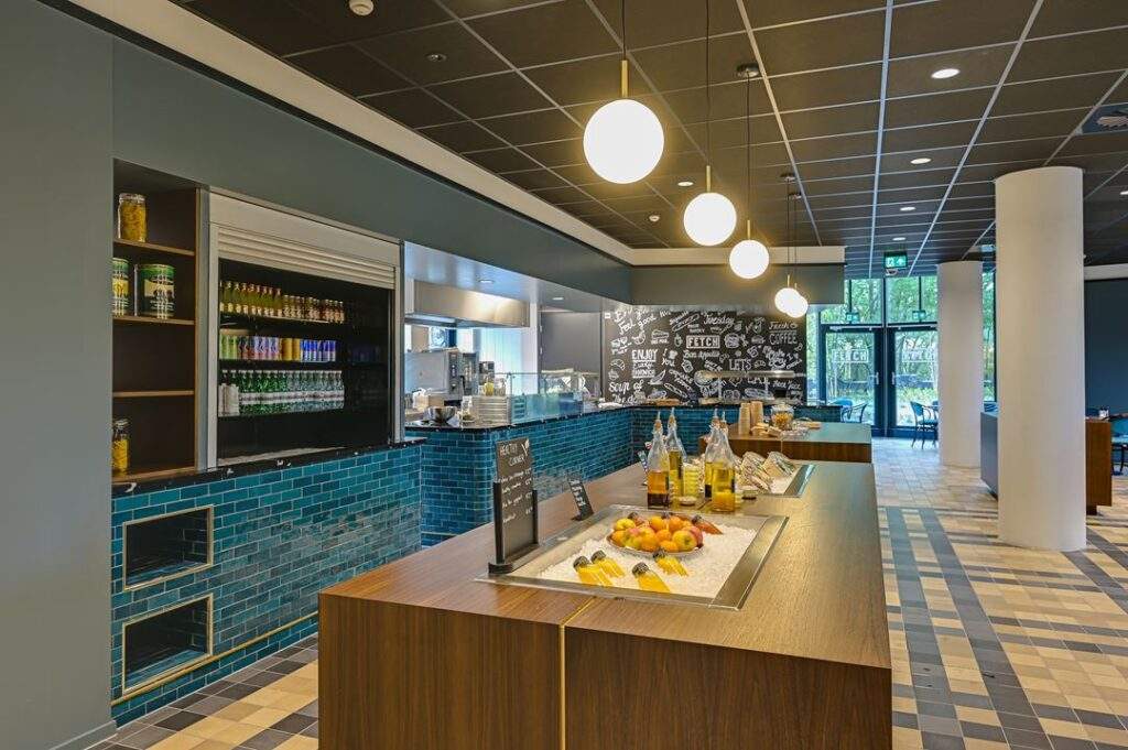 Moderne bedrijfskantine aan de Kingsfordweg met zelfbedieningsbuffet, fruit, drankjes en decoratieve wand met food-gerelateerde teksten.