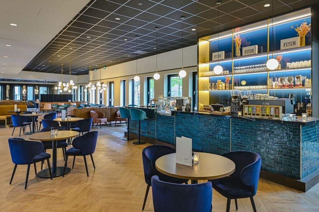Modern ingericht café met stijlvolle zitplaatsen, een blauwe betegelde bar en warme verlichting aan de Kingsfordweg.