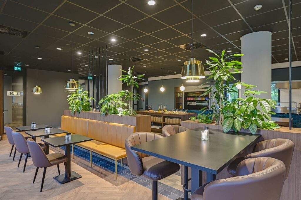 Modern ingerichte bedrijfskantine aan de Kingsfordweg met zitplaatsen, groene planten en warme verlichting.