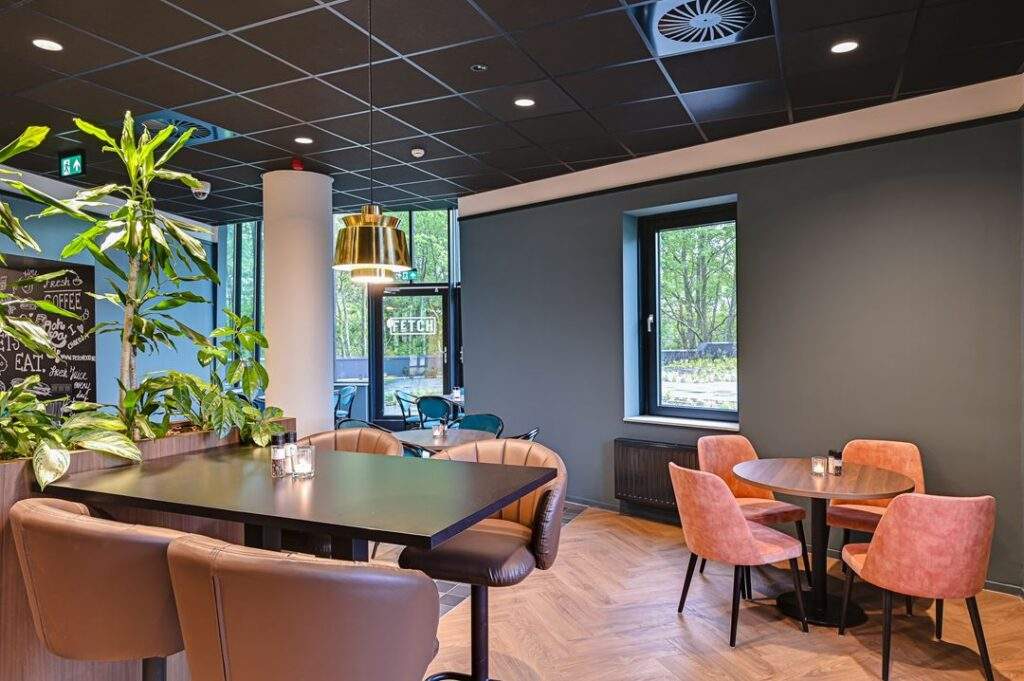 Moderne, sfeervol ingerichte lunchruimte aan de Kingsfordweg met planten, houten vloer en kleurrijke stoelen.