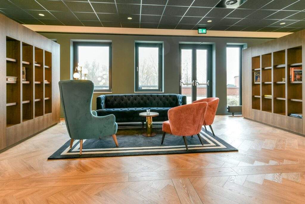 Stijlvolle loungehoek aan de Kingsfordweg met kleurrijke fauteuils, een donkere bank en houten boekenkasten.