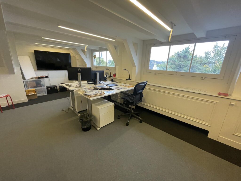 Modern office space on the Herengracht with desks, computer monitors, and a large window overlooking trees.