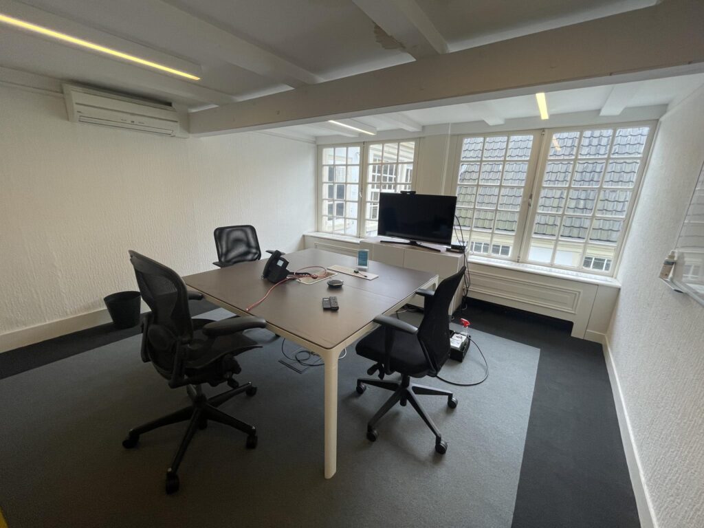 Modern meeting room at Herengracht with a conference table, office chairs, and a TV near large windows.