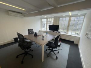 Modern meeting room at Herengracht with a conference table, office chairs, and a TV near large windows.
