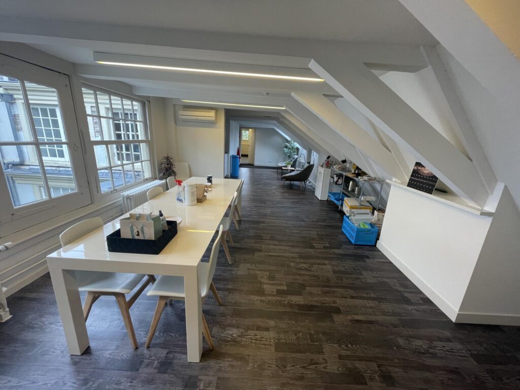 Modern office space on the Herengracht with a long white table, wooden floors, and slanted ceiling beams.