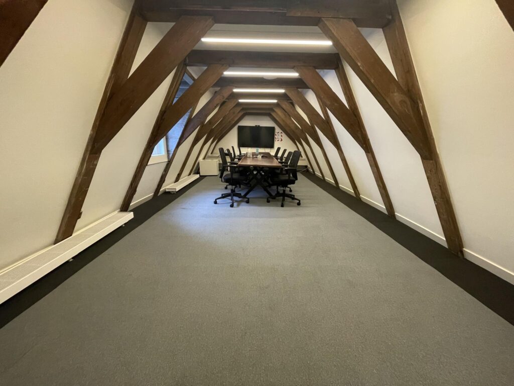 Conference room in a Herengracht attic space with wooden beams, a long table, and office chairs.