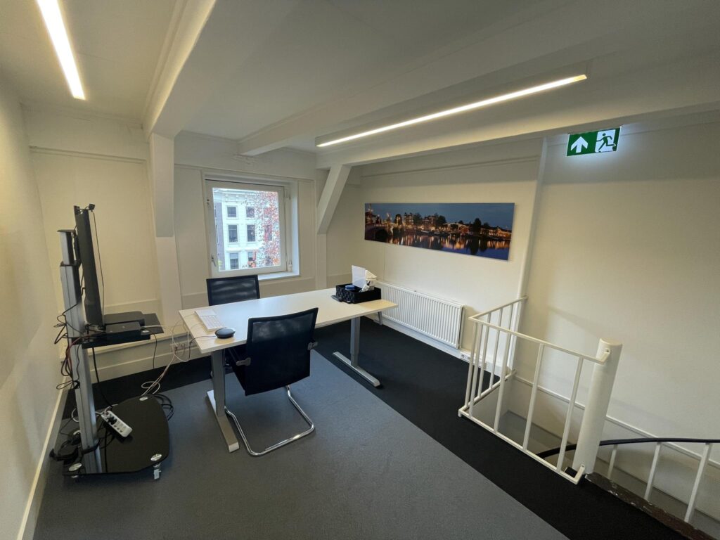 Modern office space on Herengracht with a desk setup, wall art, and a view of Amsterdam through the window.