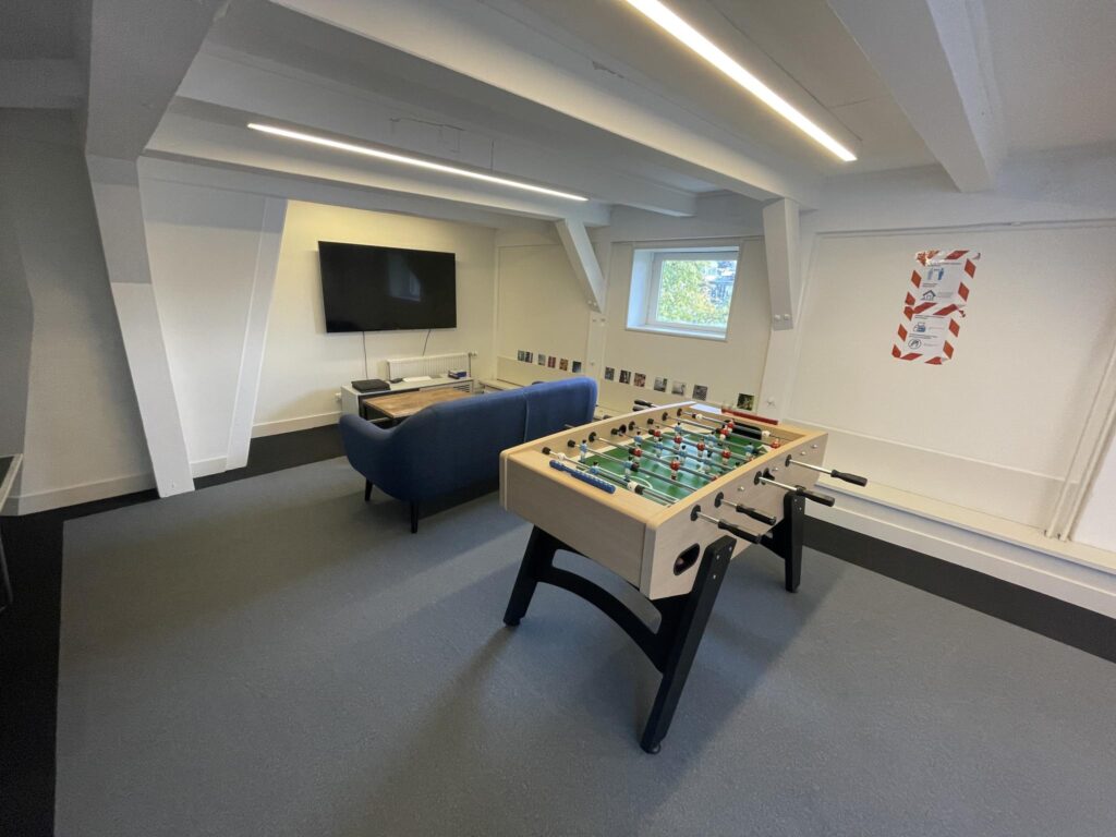Modern recreational room with a foosball table, a blue couch, and a wall-mounted TV on Herengracht.
