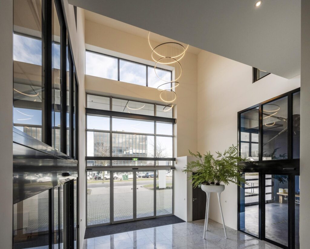 Lichte en moderne entreehal aan de Dynamostraat met hoge ramen, marmeren vloer en een opvallende designlamp.